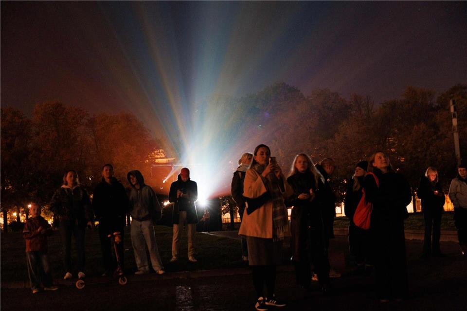 Menschen stehen vor einem Beamer, während der Berliner Dom bei der Generalprobe für das 21. Festival of Lights Berlin unter dem Motto „Let’s Shine Together“ angestrahlt wird.Carsten Koall/dpa