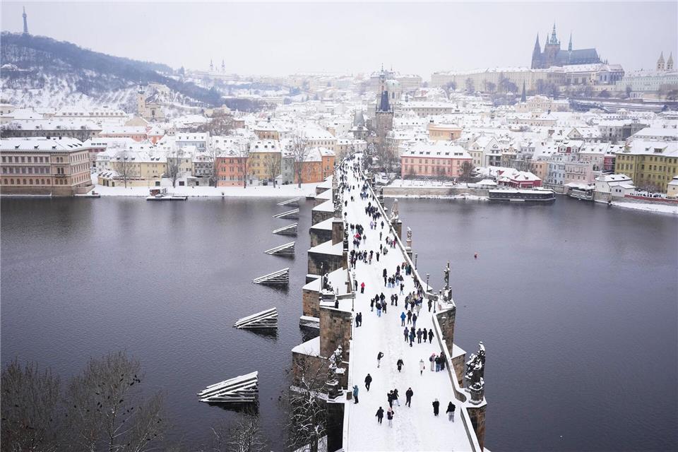Menschen überqueren die mittelalterliche Karlsbrücke nach starkem Schneefall.Petr David Josek/AP/dpa