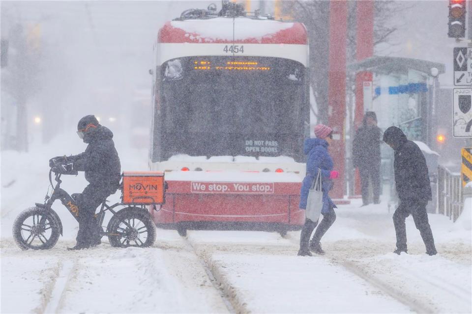 Menschen überqueren eine Straße an einem verschneiten Tag in Toronto, Kanada.Zou Zheng/XinHua/dpa