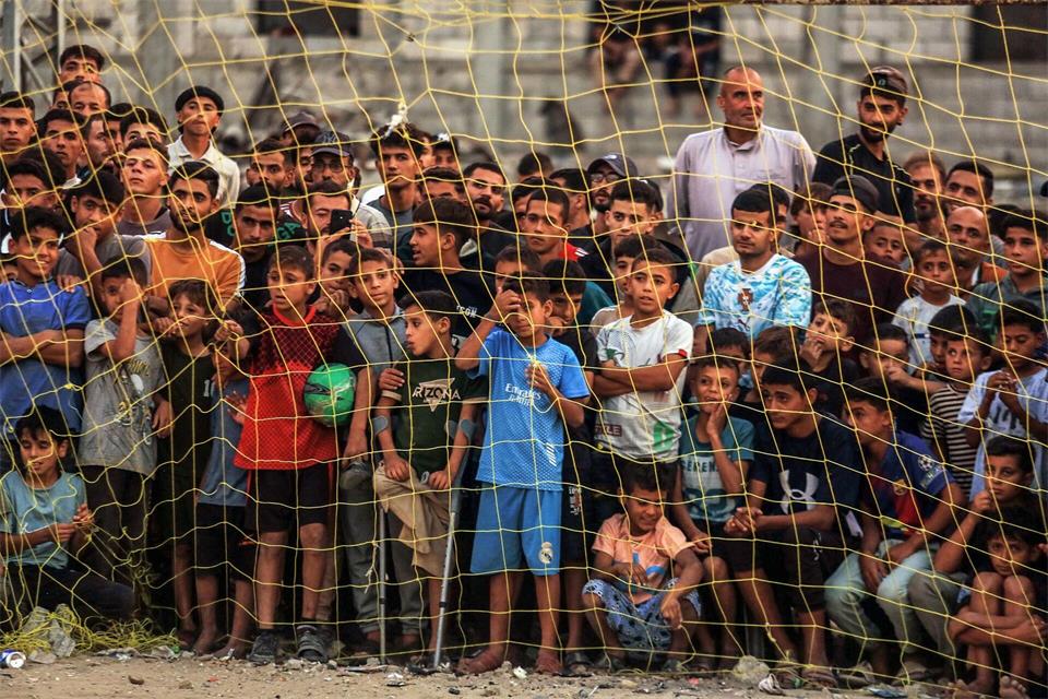 Menschen verfolgen ein Fußballspiel zwischen einer Mannschaft aus Gaza gegen eine Mannschaft aus Chan Yunis auf einem Gelände zwischen Zelten, in denen Binnenflüchtlinge untergebracht sind.Abedrahim Khatib/dpa
