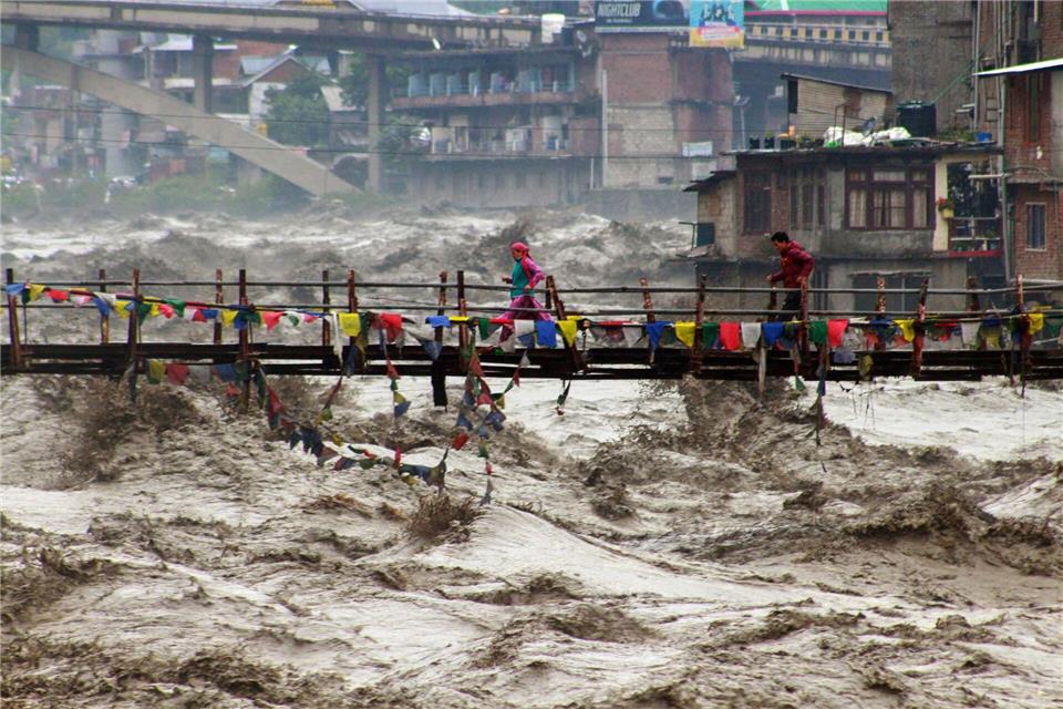 Menschen wagen im nordindischen Bundesstaat Himachal Pradesh trotz schwerer Überschwemmungen den Weg über eine Brücke, um den Fluss Beas zu überqueren.Aqil Khan/AP/dpa
