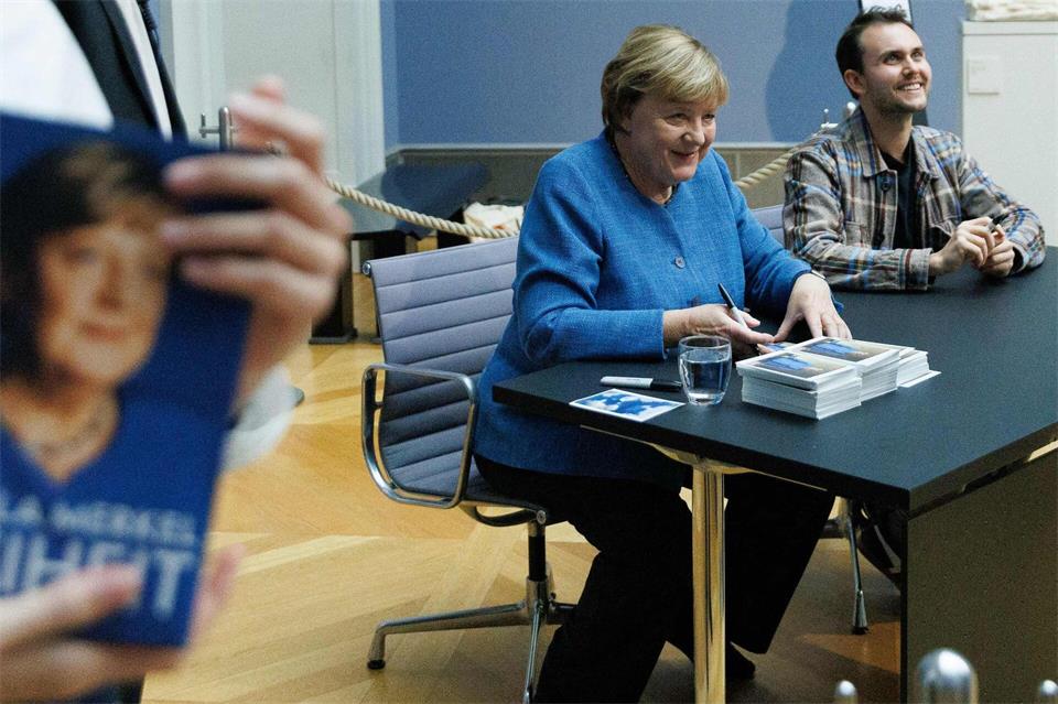 Merkel signiert Kunstpostkarten im Bode-Museum neben dem Maler ihres dort ausgestellten Porträts, Jérémie Queyras. Carsten Koall/dpa