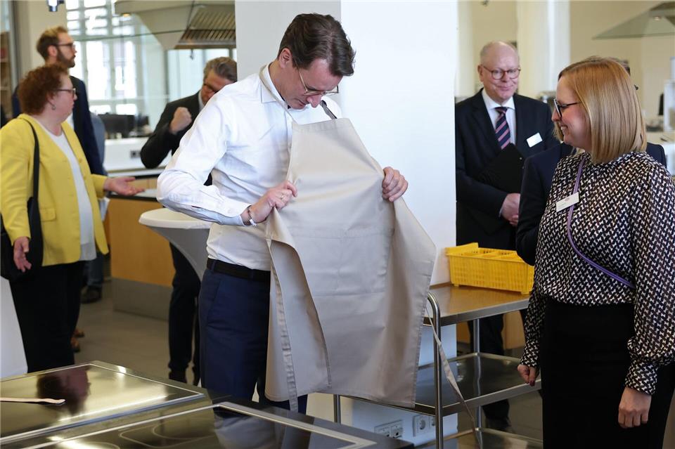 Ministerpräsident Wüst zieht sich in der Versuchsküche von Dr. Oetker eine Schürze an.Friso Gentsch/dpa