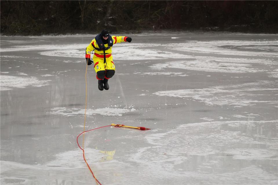 Mit einem Sprung versucht Feuerwehrmann Jannis Greve ins Eis des Öjendorfer Sees einzubrechen, um mit seinen Kameraden eine Rettung zu üben.Christian Charisius/dpa