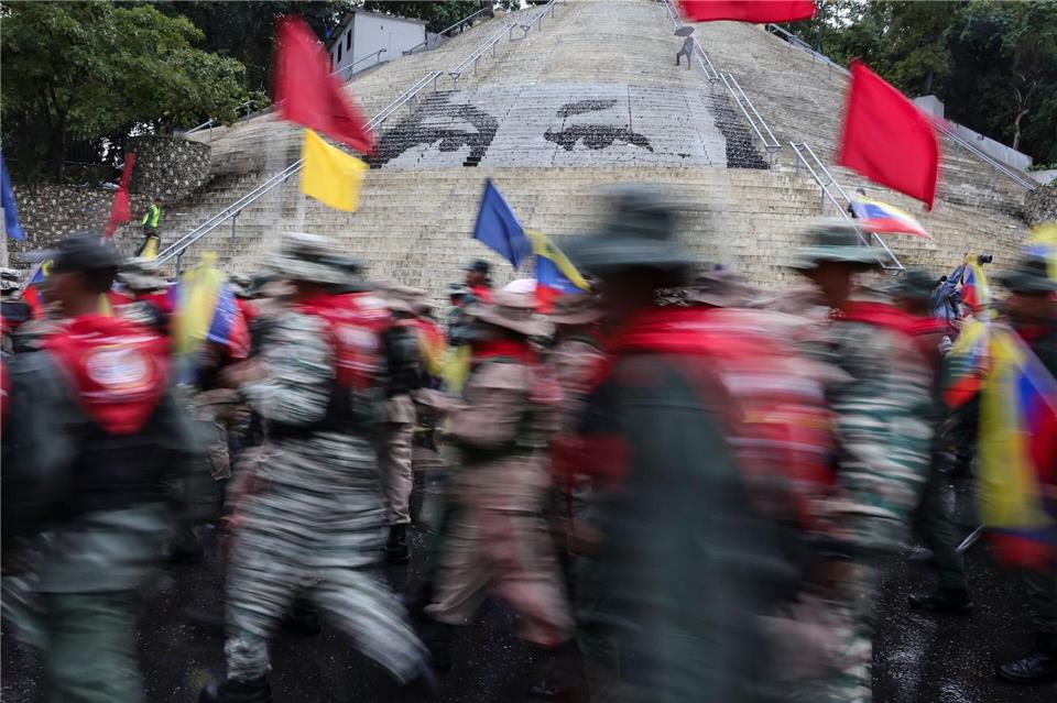 Mitglieder der Bolivarischen Miliz marschieren vor einer Treppe in Caracas, auf der die Augen des verstorbenen Präsidenten Hugo Chavez abgebildet sind, während einer Demonstration zum Gedenken an den Jahrestag der Schlacht von Santa Ines, die während des venezolanischen Bundeskriegs im 19. Jahrhundert stattfand.Jesus Vargas/dpa