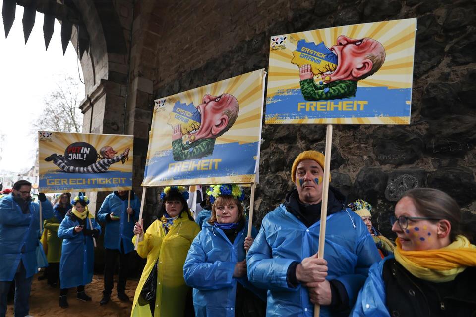 Mitglieder des ukrainischen Hilfsvereins Blau-Gelbes Kreuz halten im Kölner Rosenmontagszug Plakate mit früheren Putin-Darstellungen aus den Zügen in Köln und Düsseldorf hoch.   Oliver Berg/dpa
