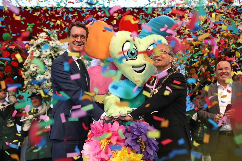Moderator Wolfram Kons (r) steht neben Ministerpräsident Hendrik Wüst (l, CDU) und Bürgermeister Reiner Breuer (m, SPD) auf der Bühne, die die Landesgartenschau eröffnen. Oliver Berg/dpa
