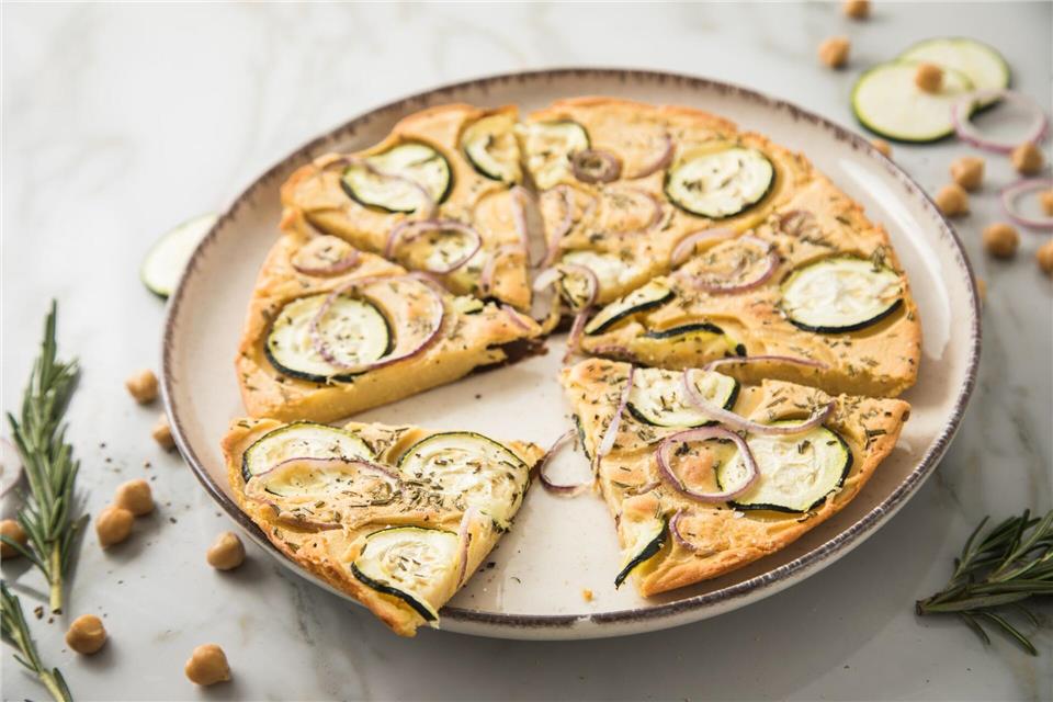 Ohne Fleisch muss bei einem Essen nicht unbedingt etwas fehlen, wie bei dieser Pizza aus Kichererbsenmehl, die mit Zucchini, Rosmarin und roten Zwiebeln belegt ist.Christin Klose/dpa-tmn