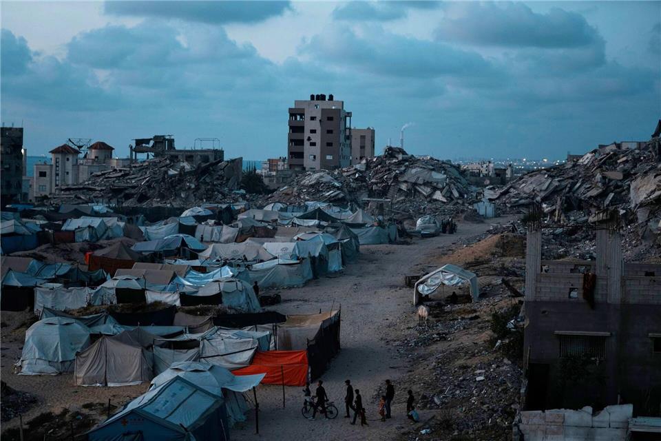 Palästinenser, die durch die israelische Luft- und Bodenoffensive auf den Gazastreifen vertrieben wurden, gehen in der Abenddämmerung über einen Platz in einem behelfsmäßigen Zeltlager.Jehad Alshrafi/AP/dpa