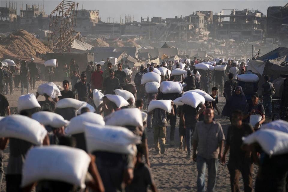 Palästinenser tragen Mehlsäcke, die von einem humanitären Hilfskonvoi auf dem Weg vom nördlichen Gazastreifen nach Gaza abgeladen wurden.Jehad Alshrafi/AP/dpa