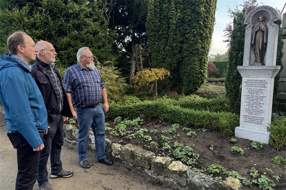 Pastor Fabian Tilling, Heinz Nienhaus vom Kirchenvorstand und Steinbildhauer Guido Löchteken betrachten den neuen Gedenkstein auf dem Raesfelder Friedhof.
