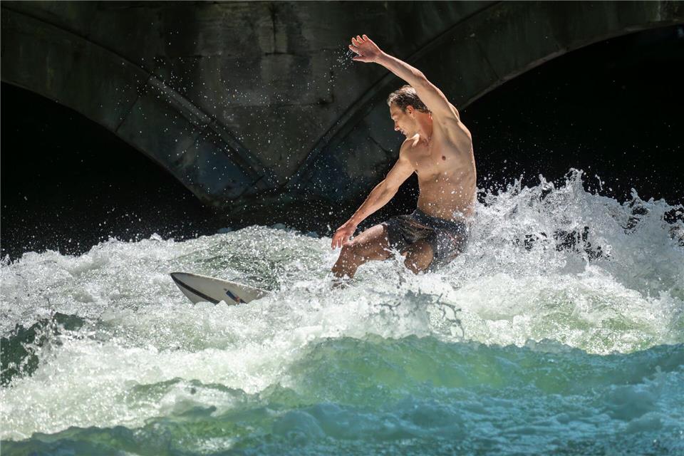Patrick surft bei sommerlichen Temperaturen mit seinem Board auf der Eisbachwelle im Englischen Garten in München.Peter Kneffel/dpa