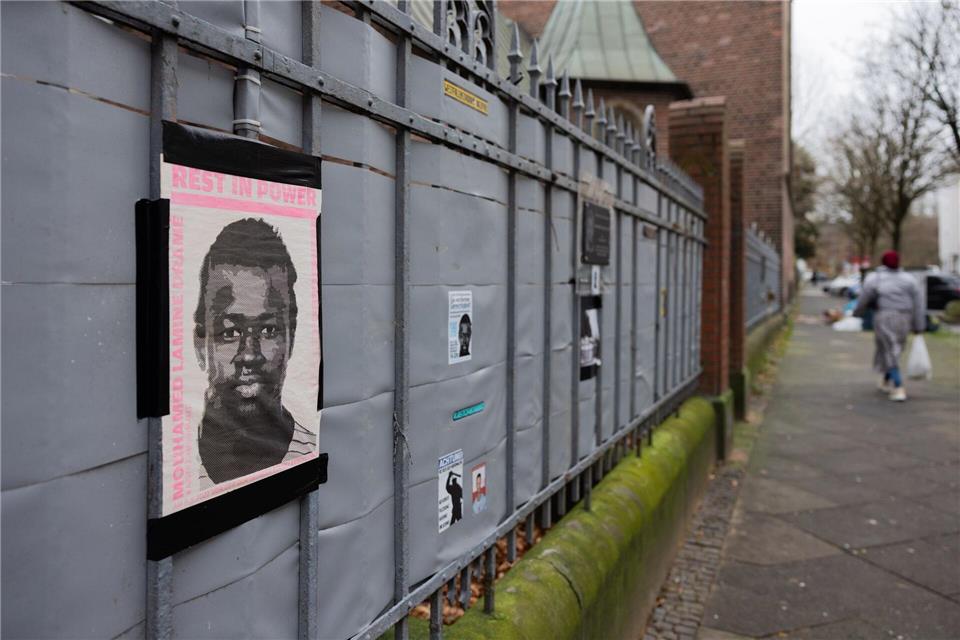 Plakate und eine Plakette erinnern am Tatort (hinter dem Zaun) an das Opfer, den 16-jährigen Senegalesen Mouhamed Drame. (Archivbild)Rolf Vennenbernd/dpa