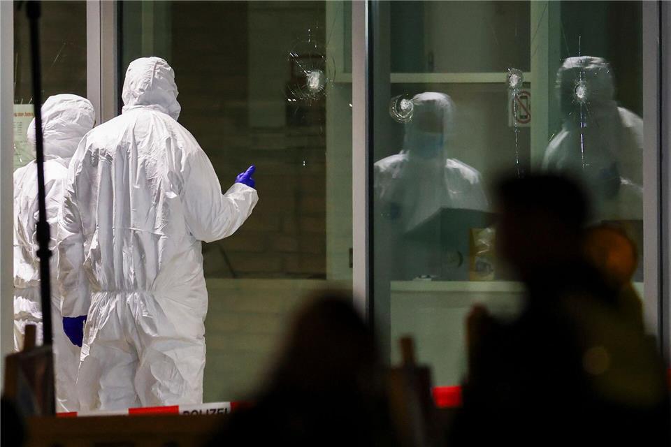 Polizeibeamte der Spurensicherung in weißen Schutzanzügen untersuchen Löcher in Glasscheiben des Kinos.Christoph Reichwein/dpa