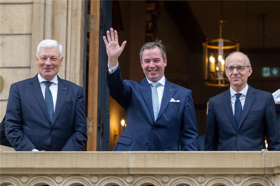 Prinz Guillaume (Mitte), Erbgroßherzog von Luxemburg, winkt nach seiner Ernennung zum „Lieutenant-Représentant“ (Ehrenleutenant) neben Luc Frieden (l), Premierminister von Luxemburg, und Jean-Claude Wiseler, Präsident des Abgeordnetenhauses, vom Balkon des Abgeordnetenhauses.Harald Tittel/dpa