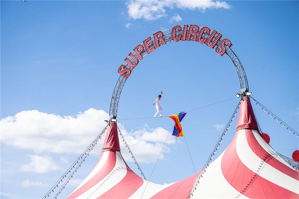 Protest in Bielefeld, Nordrhein-Westfalen: Hochseilartist David Ruiz balanciert auf einem Seil mit Regenbogenfahne über dem Zirkuszelt gegen die Haltung von Bundeskanzler Merz und Bundestagspräsidentin Klöckner.Guido Kirchner/dpa