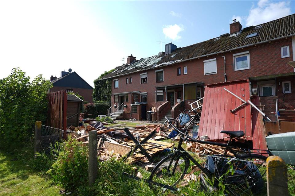 Provisorische Planen bedecken das durch ein Unwetter abgedeckte Dach eines Reihenhauses. Im Vordergrund liegen Teile einer zerstörten Gartenlaube und Dachziegel.Marcus Brandt/dpa