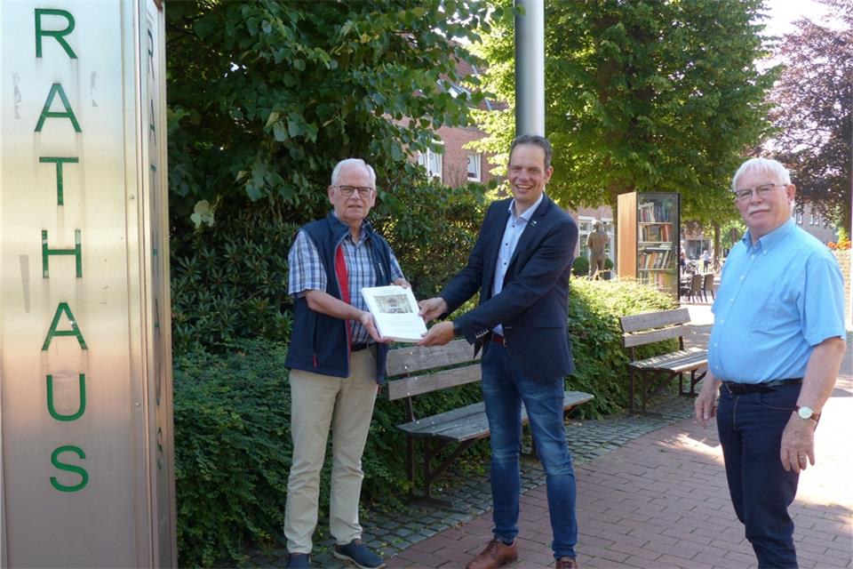 Rainer Fölting (links) und Karl-Heinz Tünte (rechts) übergeben die Chronik des Orgelbauvereins an Bürgermeister Andreas Grotendorst.