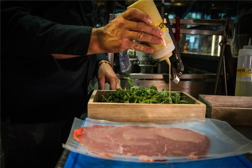 René Tepper träufelt im „The Dry Gin and Beef Club“ für ein Carpaccio eine Vinaigrette auf die Rucolablätter.Christin Klose/dpa-tmn