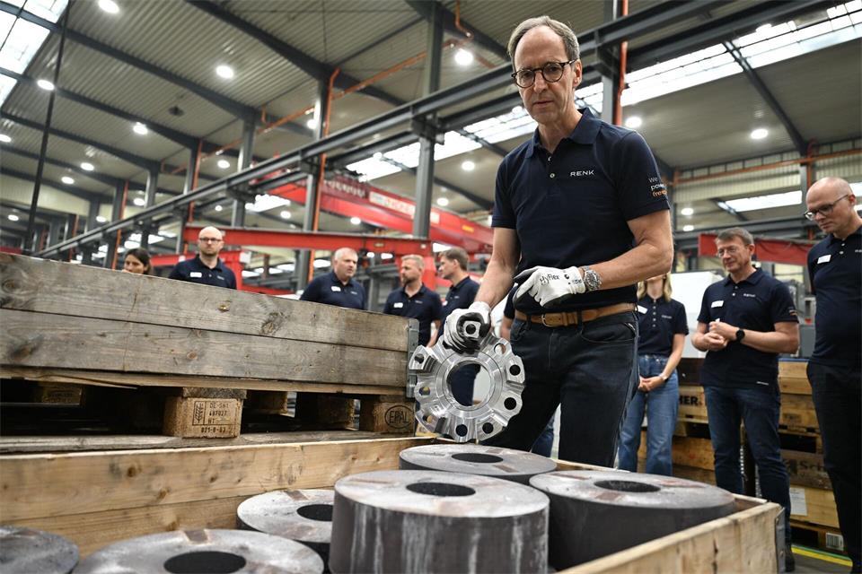 Renk-Manager Emmerich Schiller hält einen Planetenträger in der Hand, ein Bauteil für ein Panzergetriebe. Im Vordergrund sind 50 Kilo schwere Stahlscheiben zu sehen, aus denen der 15 Kilo schwere Planetenträger mit neuen Maschinen gefertigt wird.Wolf von Dewitz/dpa