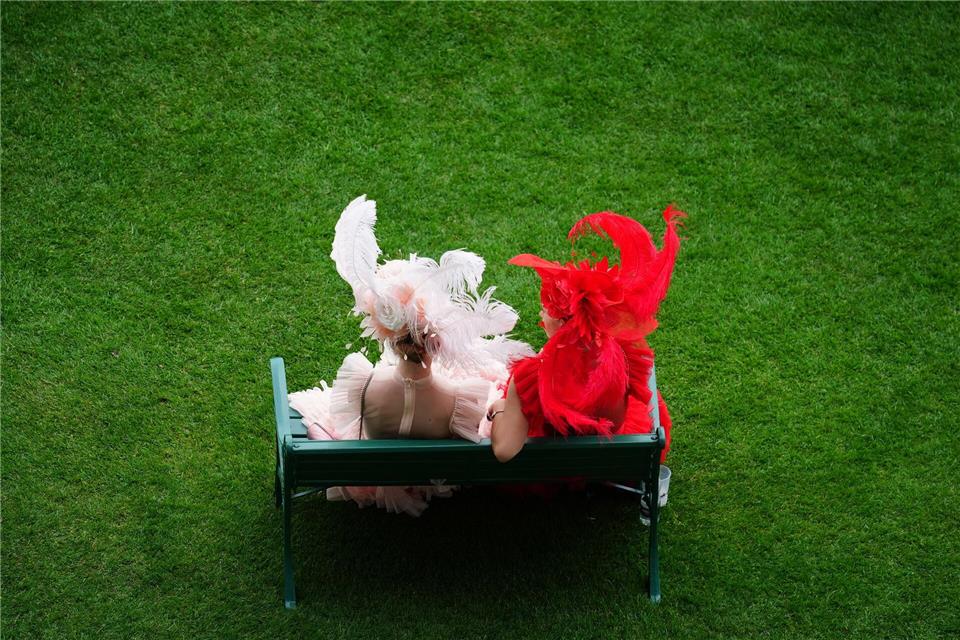 Rennbesucherinnen sitzen auf einer Bank am ersten Tag des Royal Ascot auf der Pferderennbahn von Ascot.David Davies/PA Wire/dpa