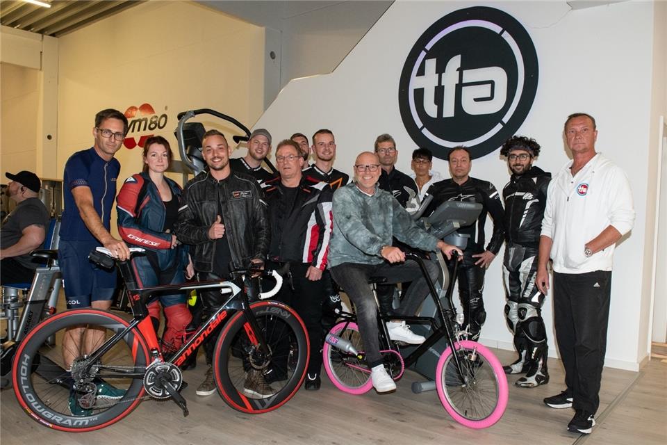Rennradfahrer Martin Brinkel (links), Sänger Olaf Henning (auf dem Fahrrad) und Andreas Rohde (rechts) helfen den Motorradfahrern bei ihrem Spendenprojekt für die Kinderkrebshilfe Weseke.