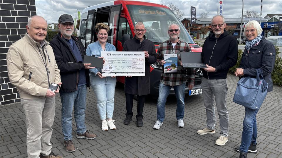 Ria Winking-Dülmer und Thomas Hatwig (3. und 4. v. li.) übergeben den symbolischen Scheck an Josef Ewering (v. li.), Stephan Emunds, Hans-Peter Schunk, Gerald Middendorf vom Vorstand des Bürgerbusvereins sowie Fahrerin Marion Wansing.