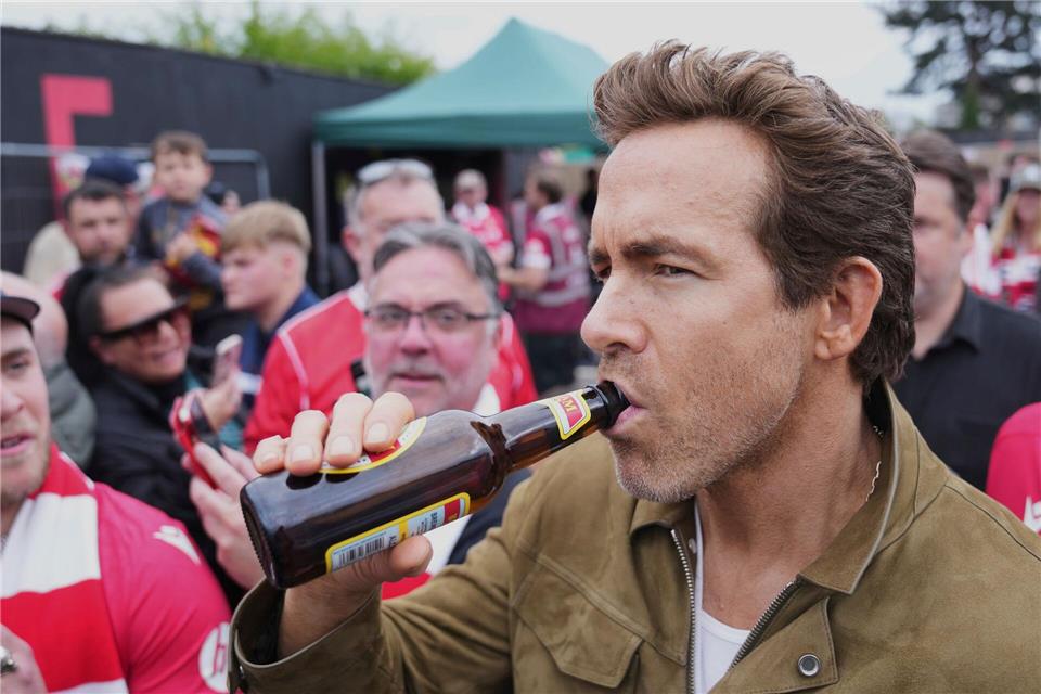 Schauspieler Ryan Reynolds lässt sich vor dem Spiel seines Clubs AFC Wrexham ein Bier schmecken.Jon Super/AP/dpa