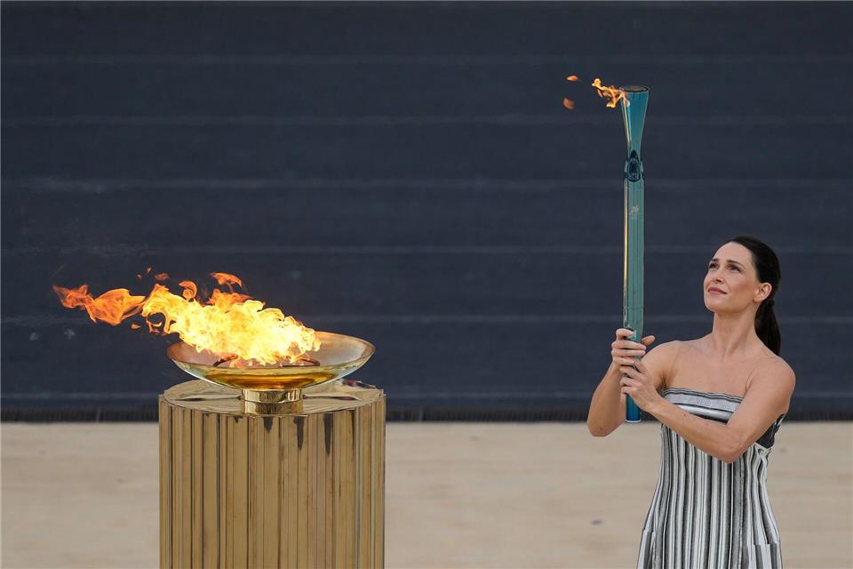 Schauspielerin Mary Mina, in der Rolle der Hohepriesterin, entzündet eine Fackel bei der Zeremonie zur Übergabe der Flamme der Olympischen Winterspiele 2026 im Panathinaikon-Stadion.Petros Giannakouris/AP/dpa