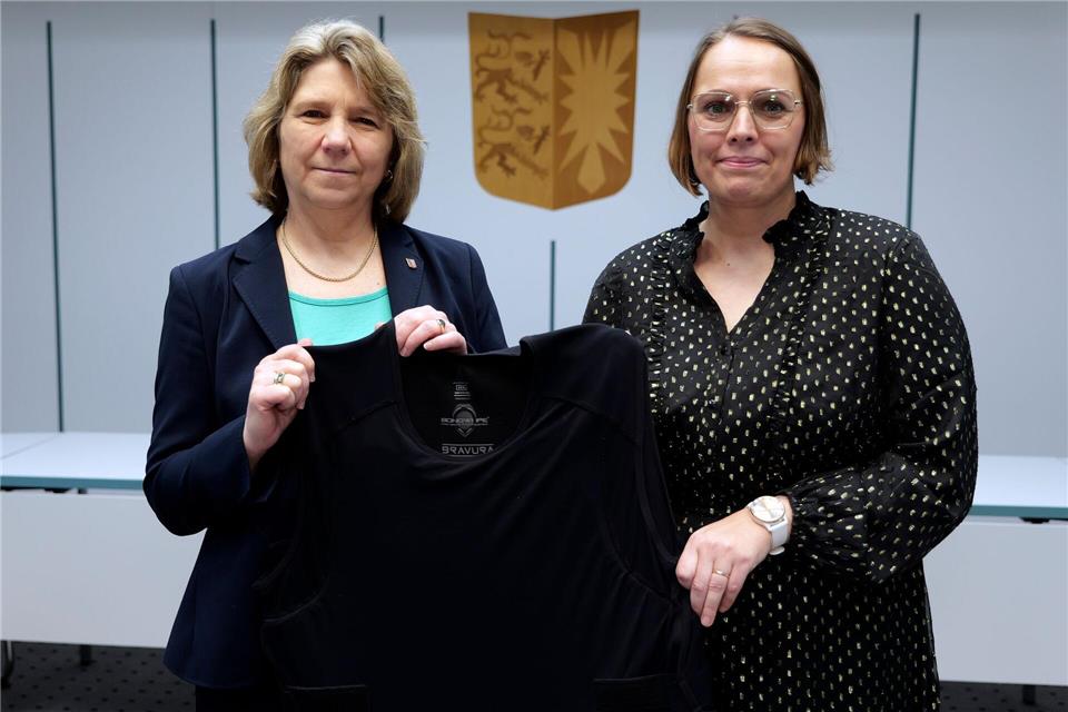 Schleswig-Holsteins Justizministerin Kerstin von der Decken (links, CDU) und die Gerichtsvollzieherin Mareile Dufke zeigen eine Schutzweste für Gerichtsvollzieher. Marcus Golejewski/dpa