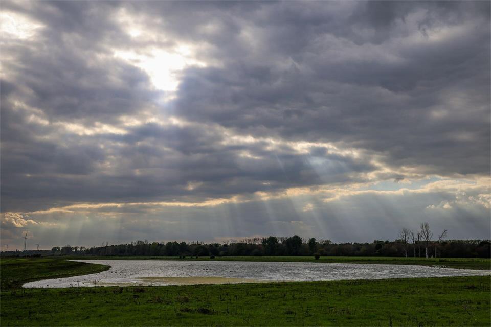 Sonnenstrahlen fallen durch die Wolken über einem kleinen See im Naturschutzgebiet Bislicher Insel.Christoph Reichwein/dpa