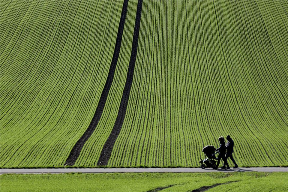 Bilder des Tages  Spaziergänger gehen im Sonnenschein an einem frisch bestellten Feld vorbei.Thomas Warnack/dpa