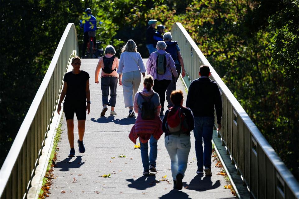 Spaziergänger laufen bei Sonnenschein über eine Brücke. Christoph Reichwein/dpa