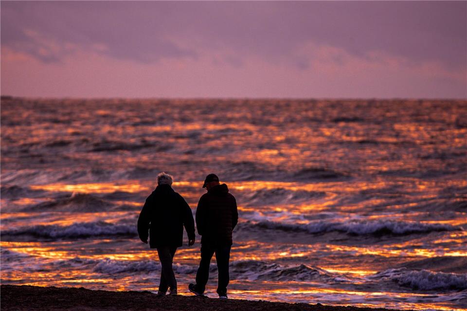 Spaziergänger sind nach Sonnenuntergang am Strand von Warnemünde an der Ostsee unterwegs.Jens Büttner/dpa