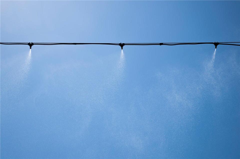 Sprinkler versprühen Wasser über der Tanzfläche einer großen Festival-Bühne.Philip Dulian/dpa