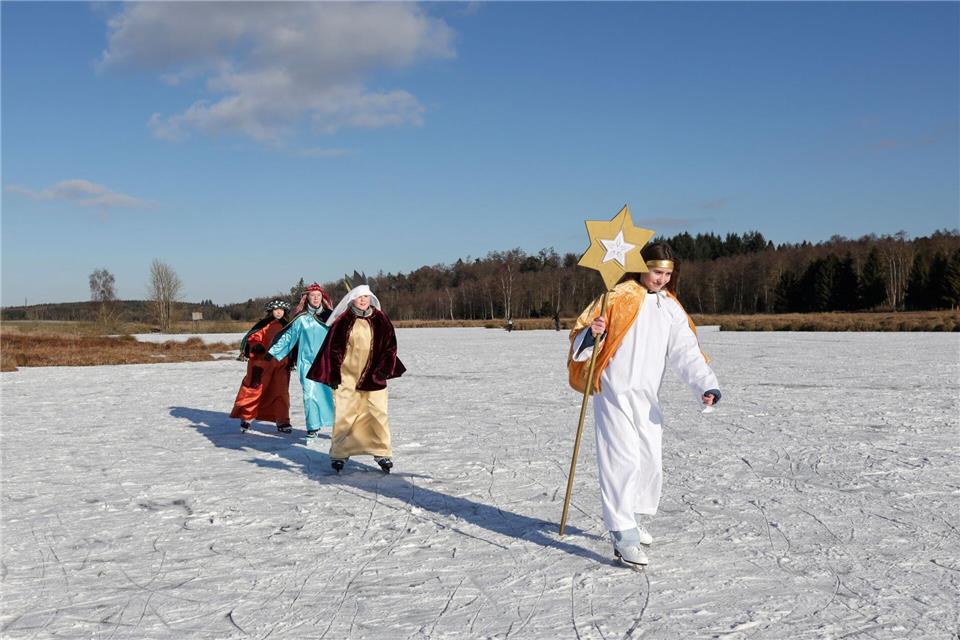 Sternsinger sind im Sonnenschein bei Betzenweiler in Tiefenbach mit Schlittschuhen auf einem zugefrorenen See unterwegs. Thomas Warnack/dpa