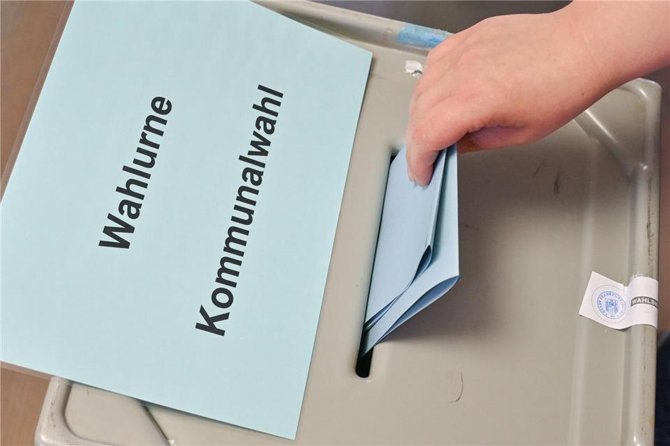 Eine Person steckt einen Zettel in die Wahlurne.