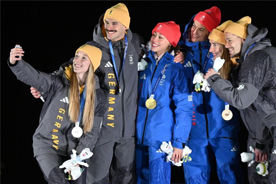 Tabitha Stoecker (Großbritannien) und Matt Weston (Großbritannien, beide M) posieren bei der Siegerehrung ihren Goldmedaillen nach dem Skeleton-Team-Wettbewerb neben Susanne Kreher (Deutschland, l) und Axel Jungk (Deutschland, 2.v.l.) mit der Silbermedaille und Jacqueline Pfeifer (Deutschland, 2.v.r.) und Christopher Grotheer (Deutschland) mit der Bronzemedaille bei den Olympischen Winterspielen Mailand Cortina 2026.Robert Michael/dpa