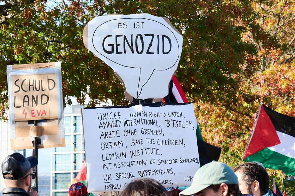 Teilnehmer einer propalästinensischen Demonstration halten ein Plakat mit dem Schriftzug „Es ist Genozid“ hoch.Annette Riedl/dpa