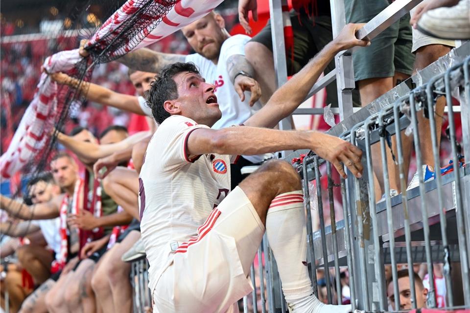 Thomas Müller steigt nach dem Bayern-Sieg auf den Zaun zu den Fans.