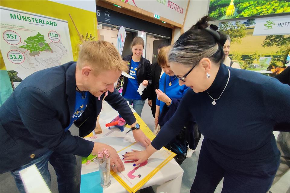 Thomas Rudde, Leader-Region Berkel-Schlinge, presst die eingefärbte Hand von Gisela Grabowski aus Geldern aufs Paper. So entsteht das rosafarbene Federkleid des Flamingos, der das Zwillbrocker Venn prägt.