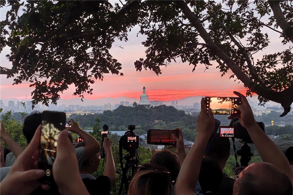 Touristen fotografieren mit ihren Handys den farbenfrohen Sonnenuntergang über der chinesischen Hauptstadt.Xing Guangli/XinHua/dpa