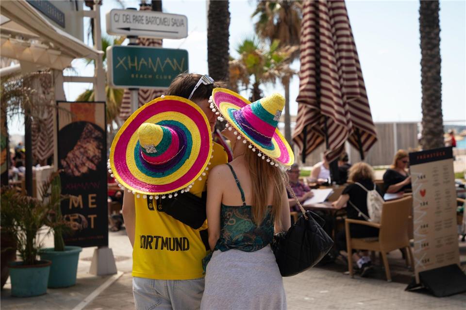 Touristen mit bunten Hüten stehen beim Start der Ballermann-Saison auf Mallorca an einer Bar.Clara Margais/dpa
