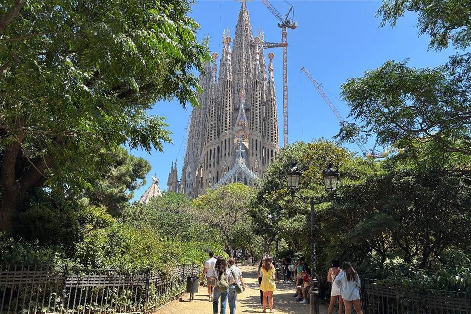 Touristen suchen bei großer Hitze den Schatten auf der Placa de la Sagrada Familia vor der gleichnamigen Basilika in Barcelona. (Archivbild)Jan Uwe Ronneburger/dpa