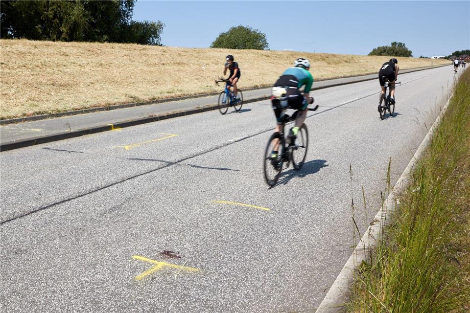 Triathleten fahren auf dem Rad an der Unglücksstelle auf dem Gauerter Hauptdeich vorbei.Georg Wendt/dpa
