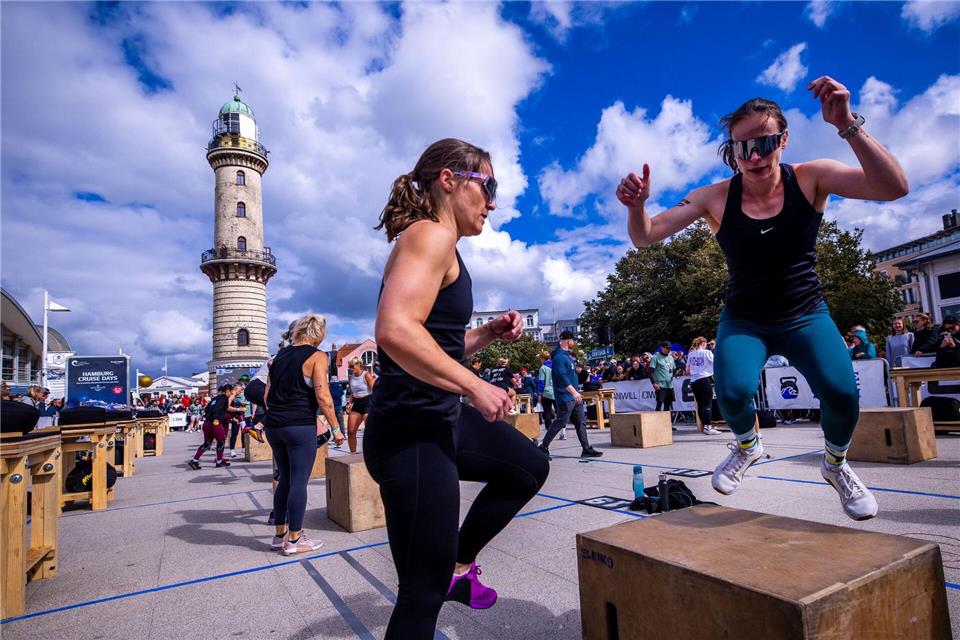 Unter dem Warnemünder Leuchtturm finden die ersten Wettkämpfe des Fitness-Events statt. Jens Büttner/dpa