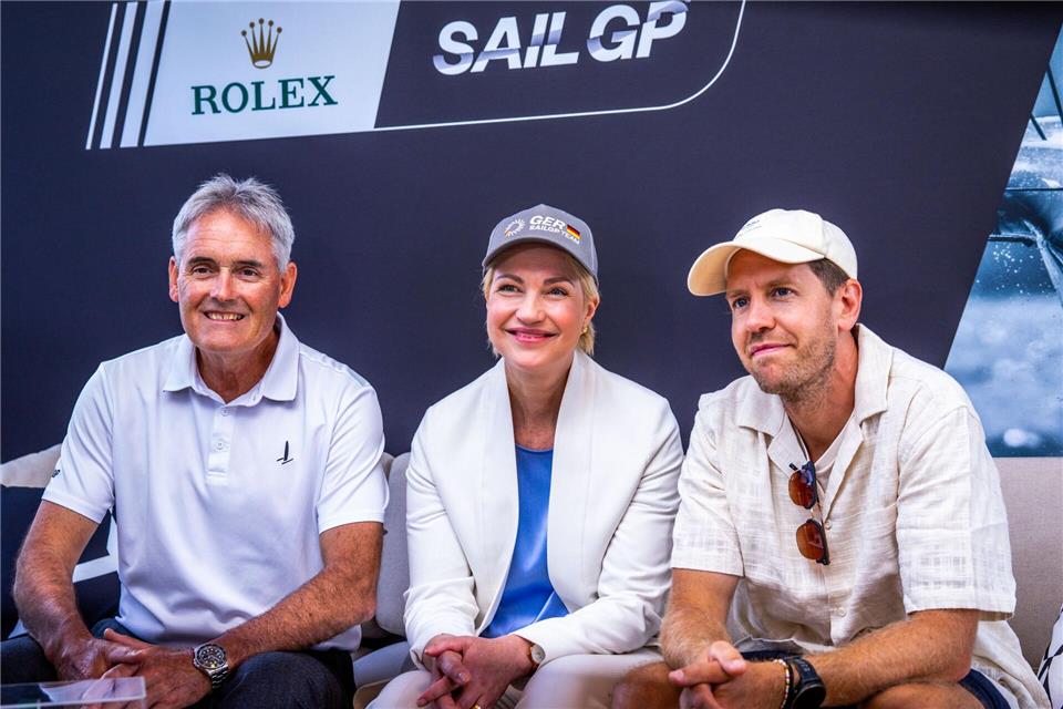 Verkündeten, dass die SailGP wieder nach Deutschland kommt: SailGP-Gründer Russell Coutts, Mecklenburgs Ministerpräsidentin Manuela Schwesig und der viermalige Formel-1-Weltmeister Sebastian Vettel. Jens Büttner/dpa