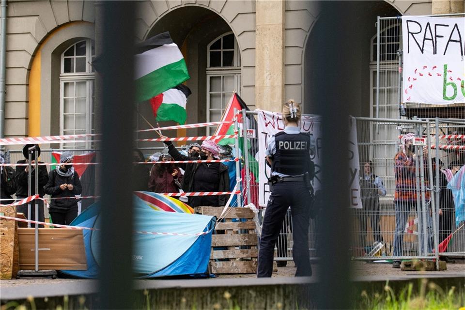 Vermummte Demonstranten stehen hinter Bauzäunen und schwenken palästinensische Fahnen.