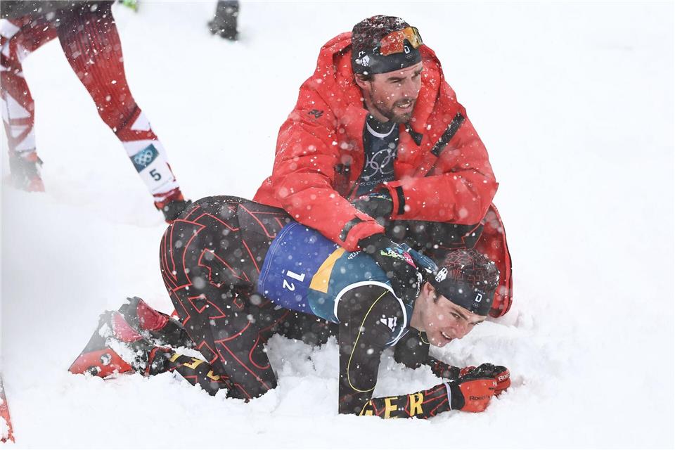 Vinzenz Geiger liegt im Schnee und wird von Teamkollege Johannes Rydzek getröstet.Daniel Karmann/dpa