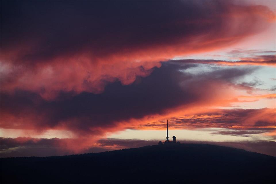Vom Sonnenaufgang rötlich verfärbt zeigt sich der Himmel über dem Brocken in Sachsen-Anhalt.Julian Stratenschulte/dpa